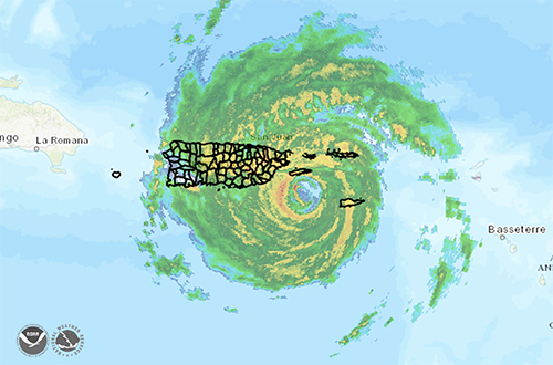 A graphic displaying a large circular storm in green and yellow overtop a black outline of an island. 