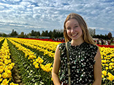 Woman standing in front of a field of yellow tulips, she is smiling at the camera.