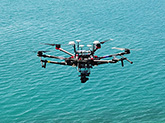 View of a mechanical flying object (drone) hovering above shallow ocean water.