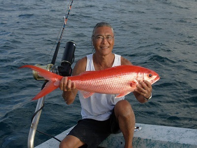 Smiling man holding big orange fish while sitting on his boat on the water.